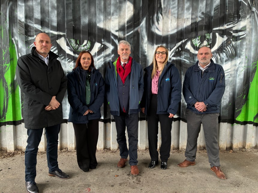 Deputy First Minister Huw Irranca‑Davies standing with council and Fly‑tipping Action Wales representatives in front of the “Don’t Waste Our Future” anti‑fly‑tipping mural created by local pupils and artist Steve Jenkins.