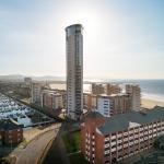 Aerial view of the Delta Hotels by Marriott Swansea in the Maritime Quarter, a red brick building in the foreground with the tall Meridian Tower behind it, Swansea Marina to the left and Swansea Bay stretching into the distance