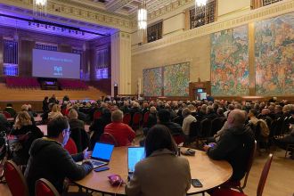 A large screen displaying “Our Blood is Black” at Brangwyn Hall during a public meeting about the Ospreys’ future.