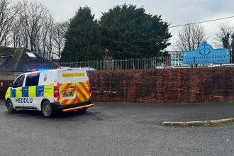 Two police vehicles parked outside Milford Haven School during a lockdown response, with the school entrance and signage visible.
