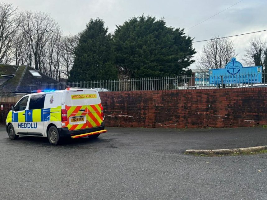 Two police vehicles parked outside Milford Haven School during a lockdown response, with the school entrance and signage visible.