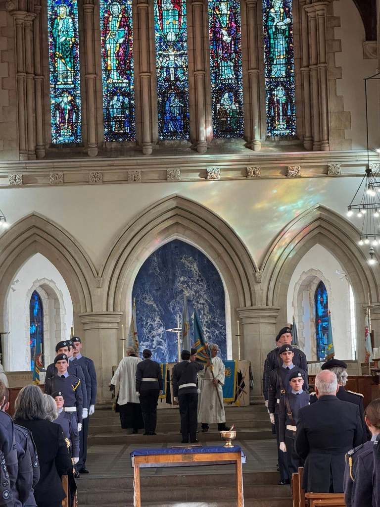 RAF Air Cadets standing in formation inside Swansea Minster beneath large stained‑glass windows during the anniversary service.