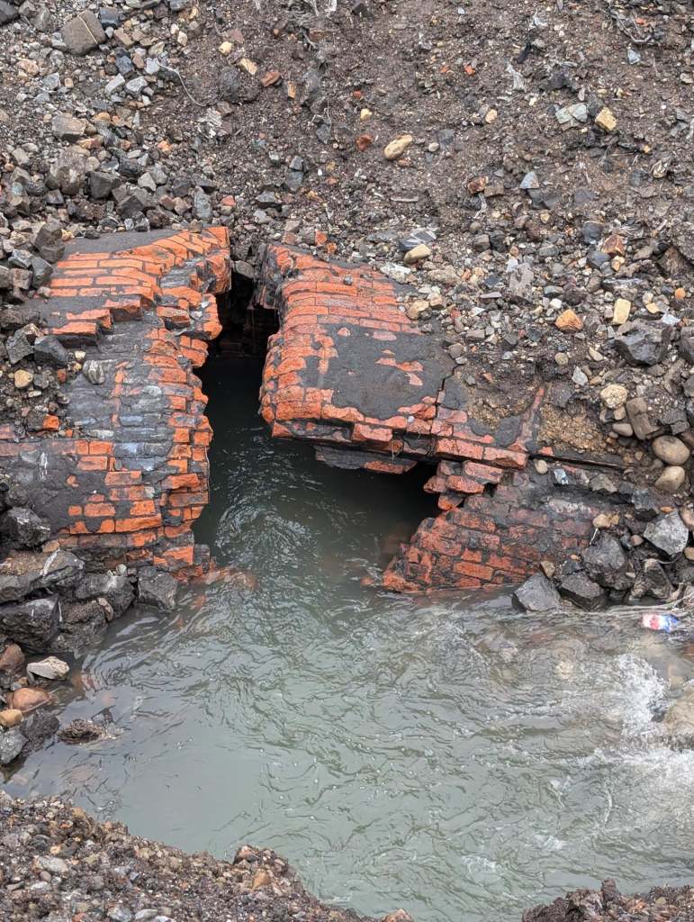 Collapsed brick tunnel with water spilling through debris at the sinkhole excavation.