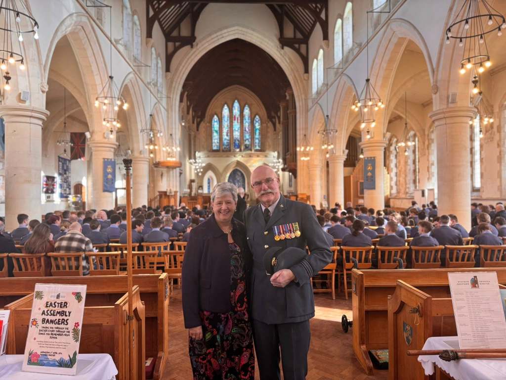 A military officer and a woman in formal attire stand inside Swansea Minster during the RAF Air Cadets anniversary service, with uniformed attendees seated behind them.