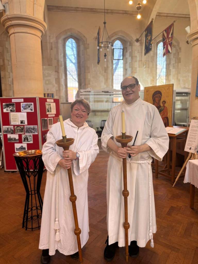 Two individuals in white robes holding tall lit candles inside Swansea Minster during the RAF Air Cadets anniversary service.