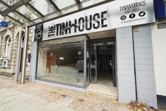 Front view of The Tinhouse taproom in Llanelli, showing the craft beer and pizzeria signage above the entrance and the interior visible through the glass frontage.