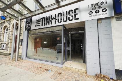 Front view of The Tinhouse taproom in Llanelli, showing the craft beer and pizzeria signage above the entrance and the interior visible through the glass frontage.