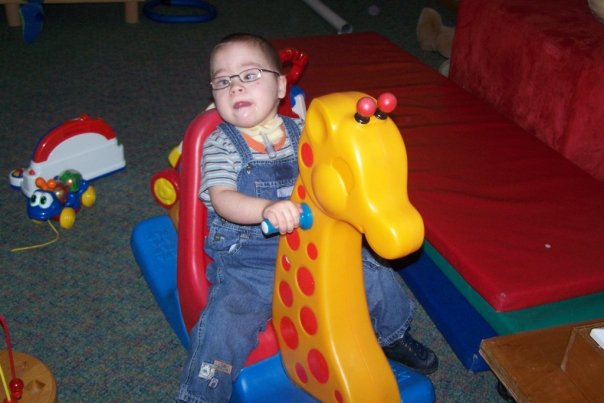 Young child wearing glasses playing on a rocking toy in a hospice playroom.