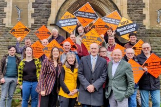 Welsh Liberal Democrat leader Jane Dodds MS with Swansea councillors Sandra Joy, Allan Jeffery and Sam Bennett in front row, surrounded by party supporters holding orange Liberal Democrat campaign signs at Brynmill Community Centre