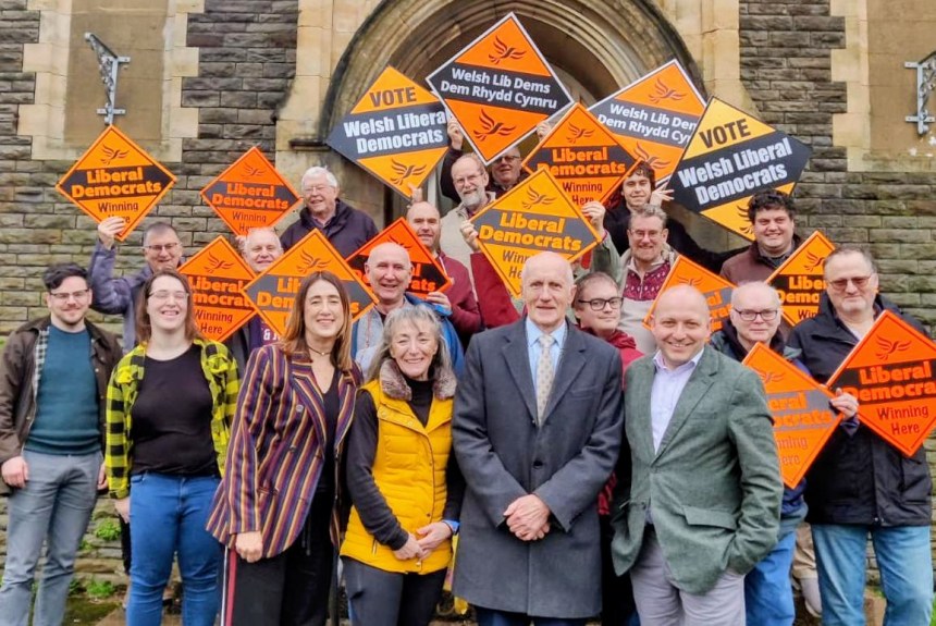 Welsh Liberal Democrat leader Jane Dodds MS with Swansea councillors Sandra Joy, Allan Jeffery and Sam Bennett in front row, surrounded by party supporters holding orange Liberal Democrat campaign signs at Brynmill Community Centre