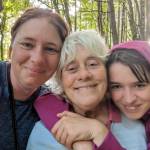 Three family members smiling together during an outdoor walk in woodland.