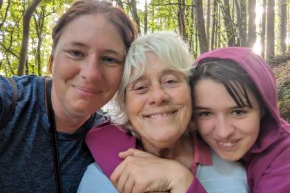 Three family members smiling together during an outdoor walk in woodland.