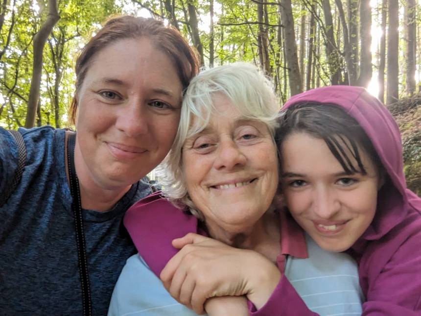 Three family members smiling together during an outdoor walk in woodland.