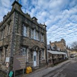 Stone-built Maesteg Hospital with Gothic features, showing main entrance and outpatient signage under cloudy sky.