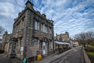 Stone-built Maesteg Hospital with Gothic features, showing main entrance and outpatient signage under cloudy sky.