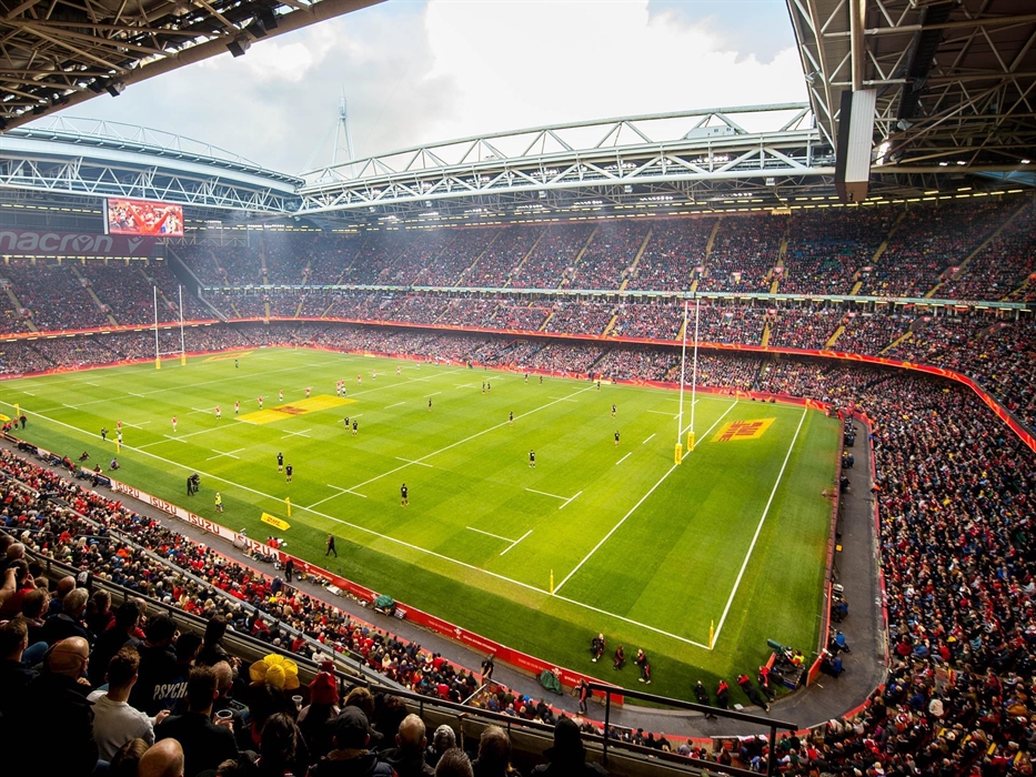 View inside a full Principality Stadium during a rugby match, with players on the pitch and stands packed with supporters.