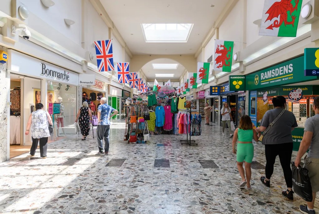 Interior of Aberafan Shopping Centre with shoppers walking past stores and clothing displays.