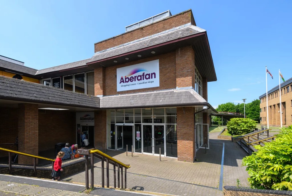 Exterior view of Aberafan Shopping Centre with bilingual signage and shoppers entering the building.