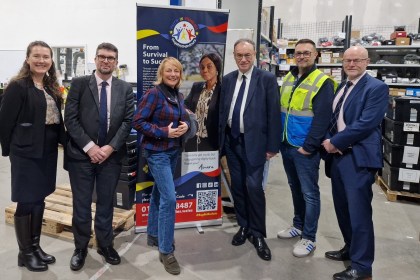 Group photo of Andrew Bailey, Cherrie Bija and staff standing in front of a Faith in Families banner inside the Cwtch Mawr Multibank.