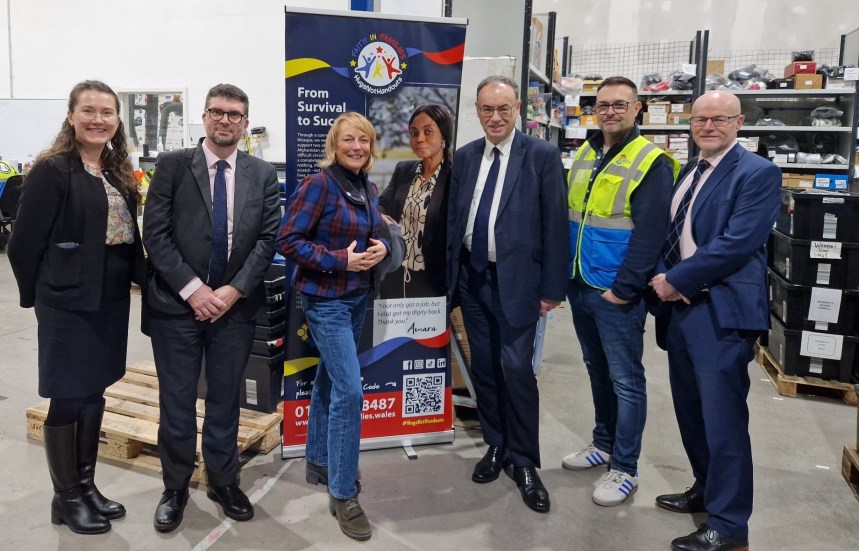 Group photo of Andrew Bailey, Cherrie Bija and staff standing in front of a Faith in Families banner inside the Cwtch Mawr Multibank.