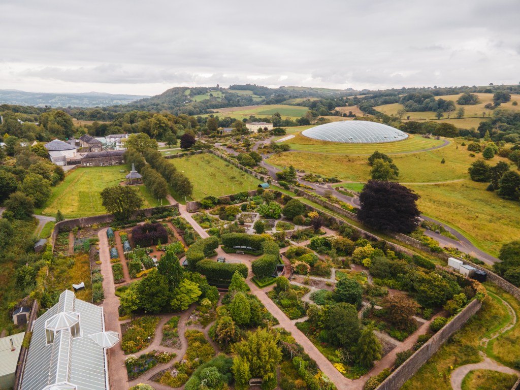 Drone image looking down on the Great Glasshouse and landscaped gardens, with pathways, planting areas and green spaces visible across the site.