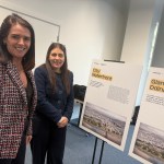 Two women standing beside display boards showing information and aerial images of the proposed City Waterfront redevelopment at a public exhibition.