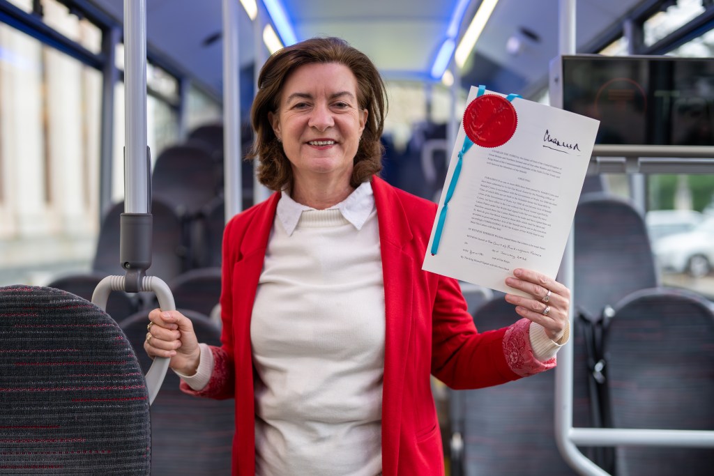 First Minister Eluned Morgan standing inside a Transport for Wales bus, holding up the Bus Services Act document.