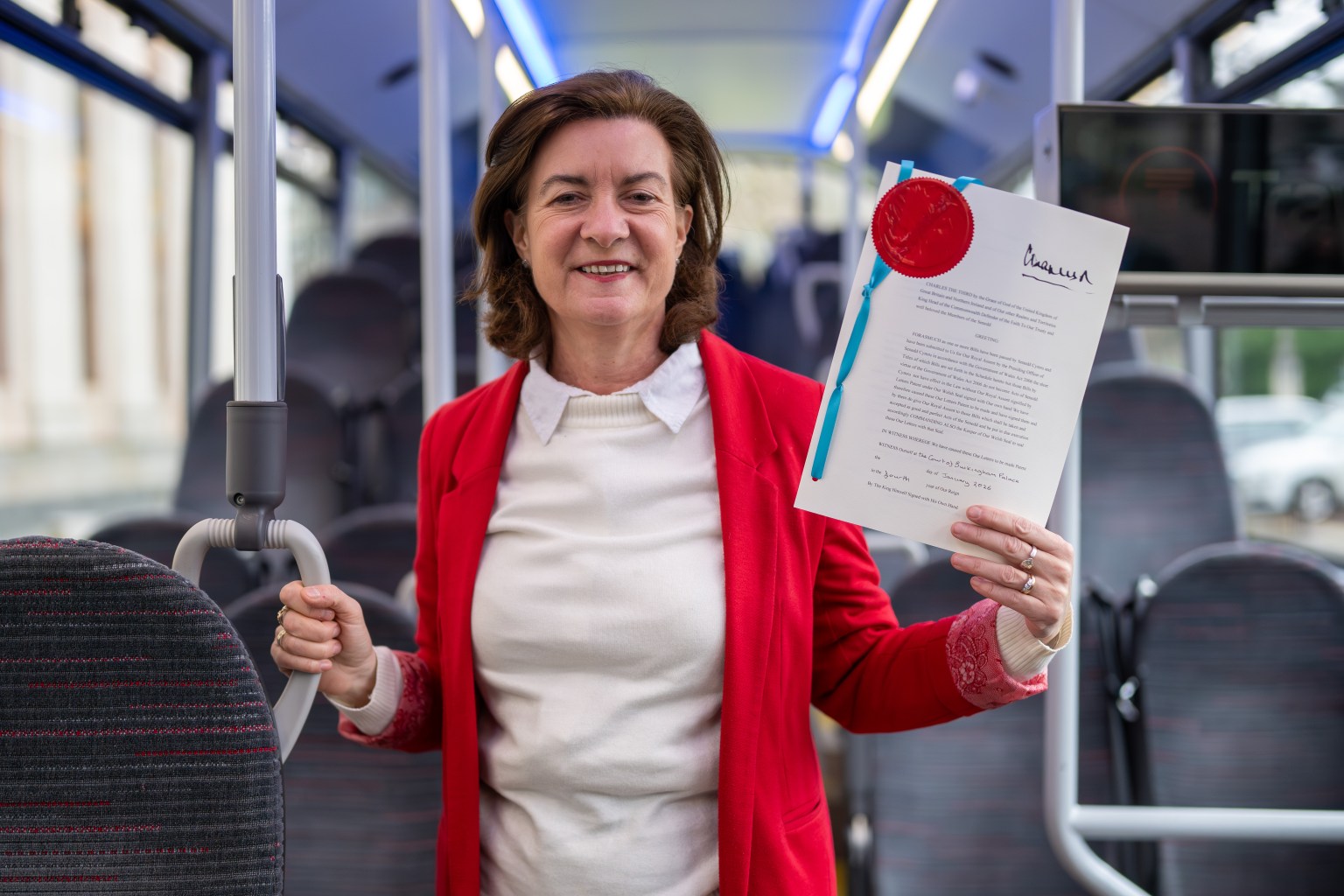 First Minister Eluned Morgan standing inside a Transport for Wales bus, holding up the Bus Services Act document.