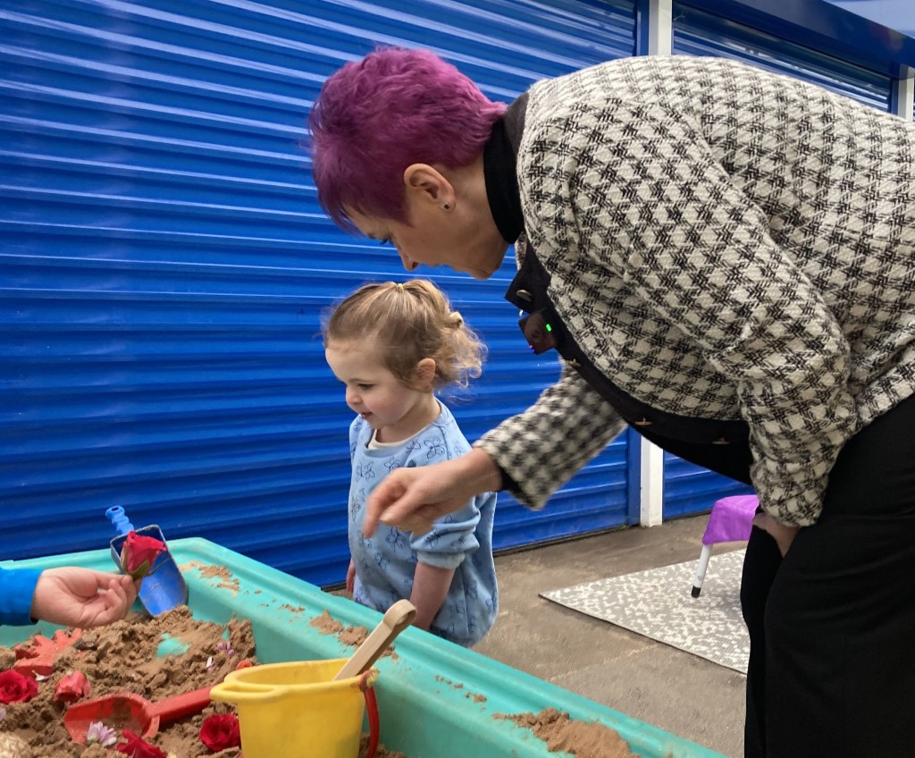 Minister Dawn Bowden engaging with a child at a sand play table during a Flying Start visit in Swansea.