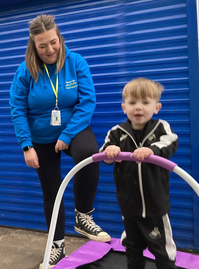 Young child on a small trampoline with a staff member supervising at a Flying Start childcare setting.