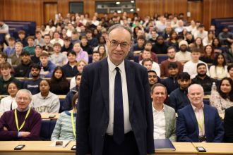 Andrew Bailey standing at the front of a full lecture hall, addressing Swansea University students during a Q&A session.