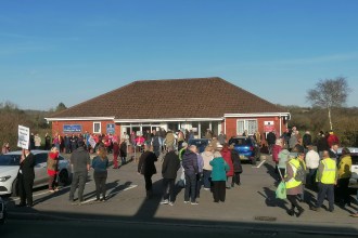 Large crowd of over 100 people gathered in the car park outside Meddygfa'r Sarn surgery in Pontyates holding protest signs against its proposed closure