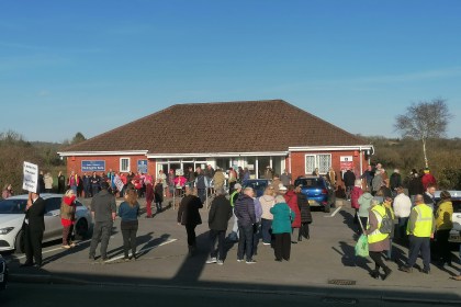 Large crowd of over 100 people gathered in the car park outside Meddygfa'r Sarn surgery in Pontyates holding protest signs against its proposed closure