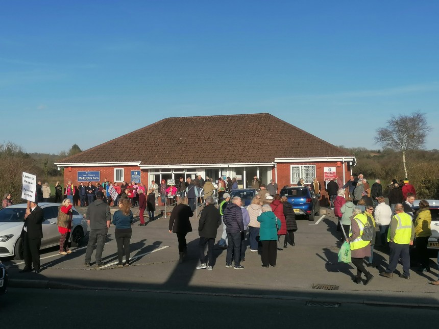 Large crowd of over 100 people gathered in the car park outside Meddygfa'r Sarn surgery in Pontyates holding protest signs against its proposed closure