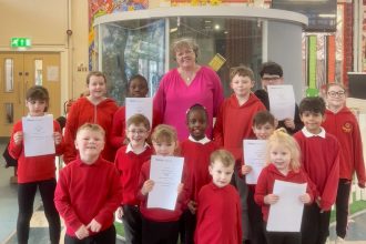 Group of Craigfelen Primary pupils in red uniforms holding certificates alongside a member of staff in a classroom.