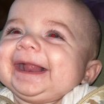 Smiling baby boy wearing a patterned outfit, pictured in a family photo.