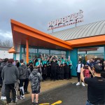 Popeyes staff in teal uniforms celebrating outside the new Llanelli restaurant during the grand opening, with crowds gathered around the entrance.
