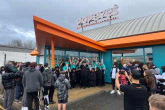 Popeyes staff in teal uniforms celebrating outside the new Llanelli restaurant during the grand opening, with crowds gathered around the entrance.