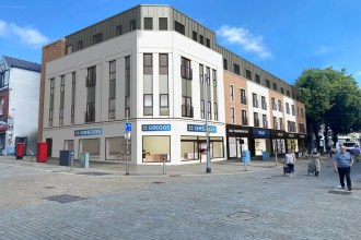 CGI rendering of the refurbished 254-260 Oxford Street building in Swansea showing modern shop frontages including Greggs bakery on the ground floor with apartments above