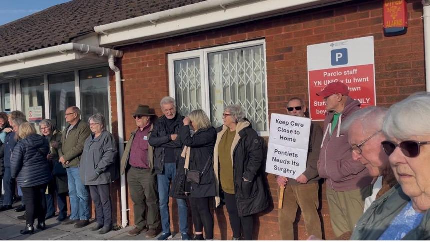 Residents forming a human chain outside Meddygfa'r Sarn surgery in Pontyates holding protest banners against its proposed closure
