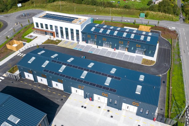 Drone image of the Parc Gelli Werdd commercial site in Cross Hands, featuring blue‑roofed business units with solar panels, numbered bays, parking areas and surrounding roads.