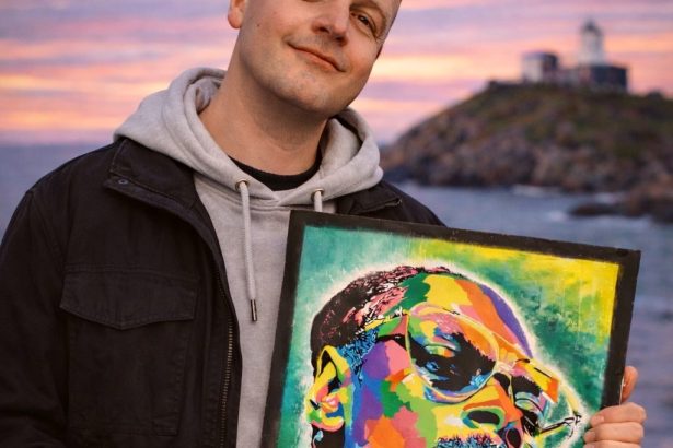 Swansea artist standing outdoors at sunset holding a colourful pop‑art portrait of Snoop Dogg as part of the Six Degree Artist project.