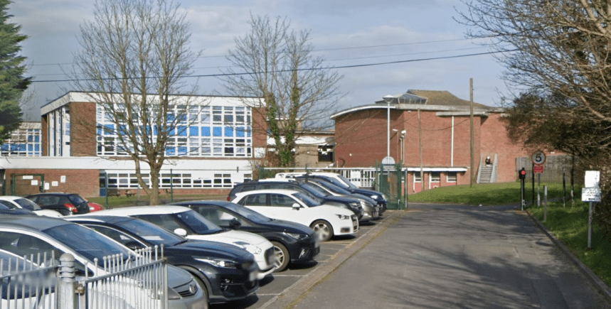 Exterior view of Milford Haven Comprehensive School with car park, gated entrance and school buildings.