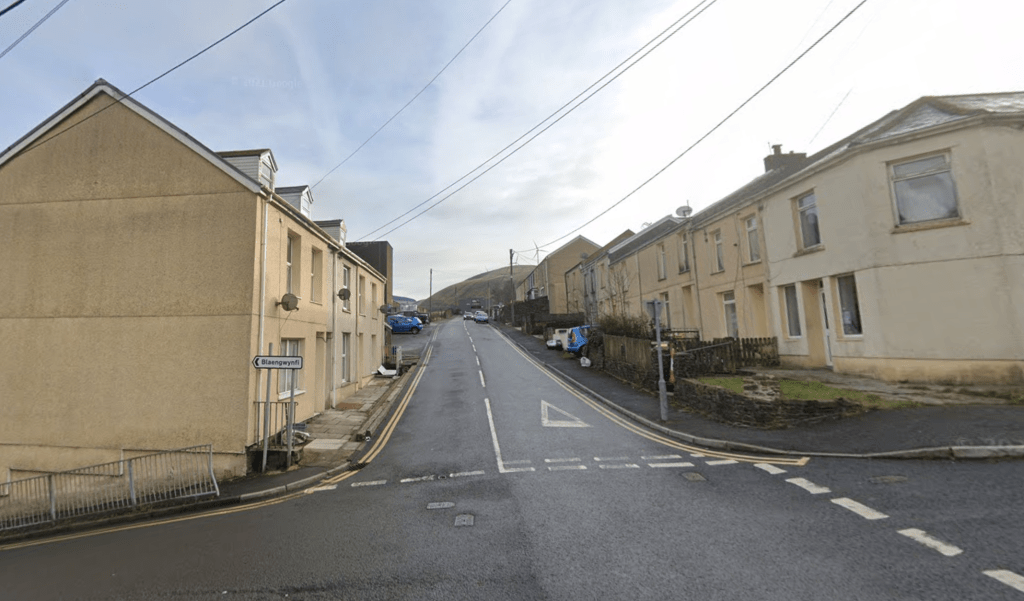 View of Commercial Street in Abergwynfi with terraced houses and parked cars, where police are dealing with an ongoing incident.