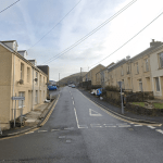 View of Commercial Street in Abergwynfi with terraced houses and parked cars, where police are dealing with an ongoing incident.