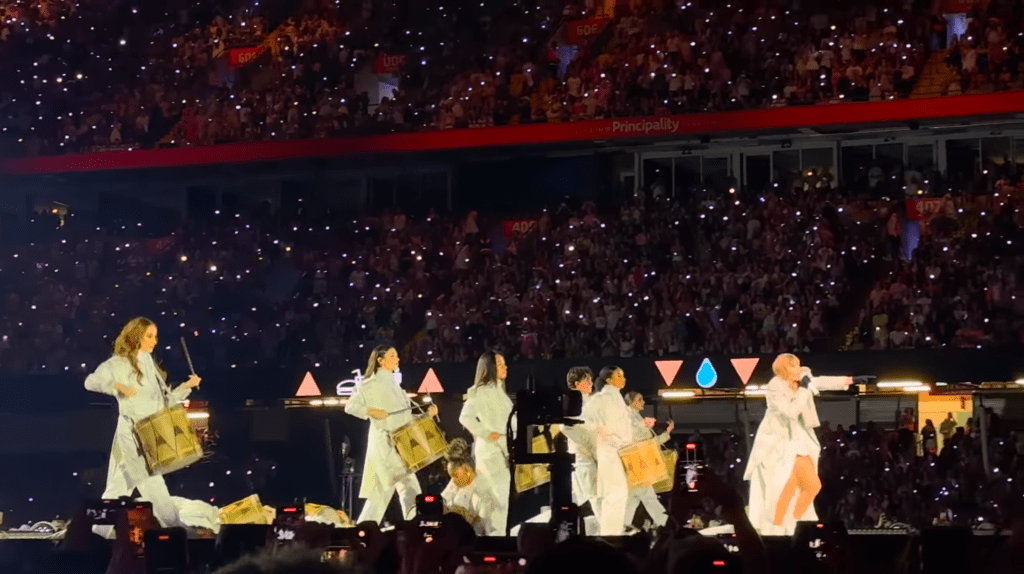 Taylor Swift performing on a central stage at Cardiff’s Principality Stadium during the 2024 Eras Tour, surrounded by a full crowd.