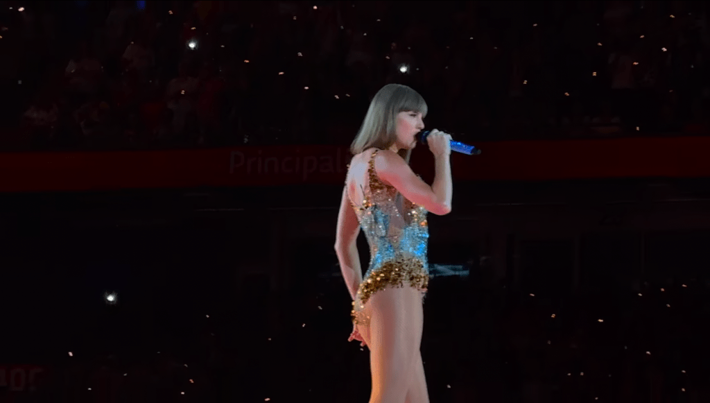Taylor Swift singing on stage in a sequinned outfit during her 2024 Eras Tour performance at Cardiff’s Principality Stadium.