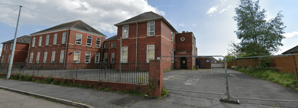 Side view of the former Stebonheath School in Llanelli, showing boarded windows, fencing and the entrance driveway.