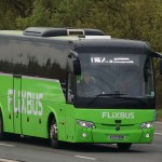 A green FlixBus coach travelling along a rural highway, displaying a digital destination sign for London.