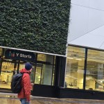 Exterior of Y Storfa showing vertical garden wall, glass windows, and entrance with pedestrian passing by.